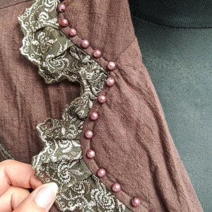 May include: A brown jacket with a lace trim and pink beads around the collar.