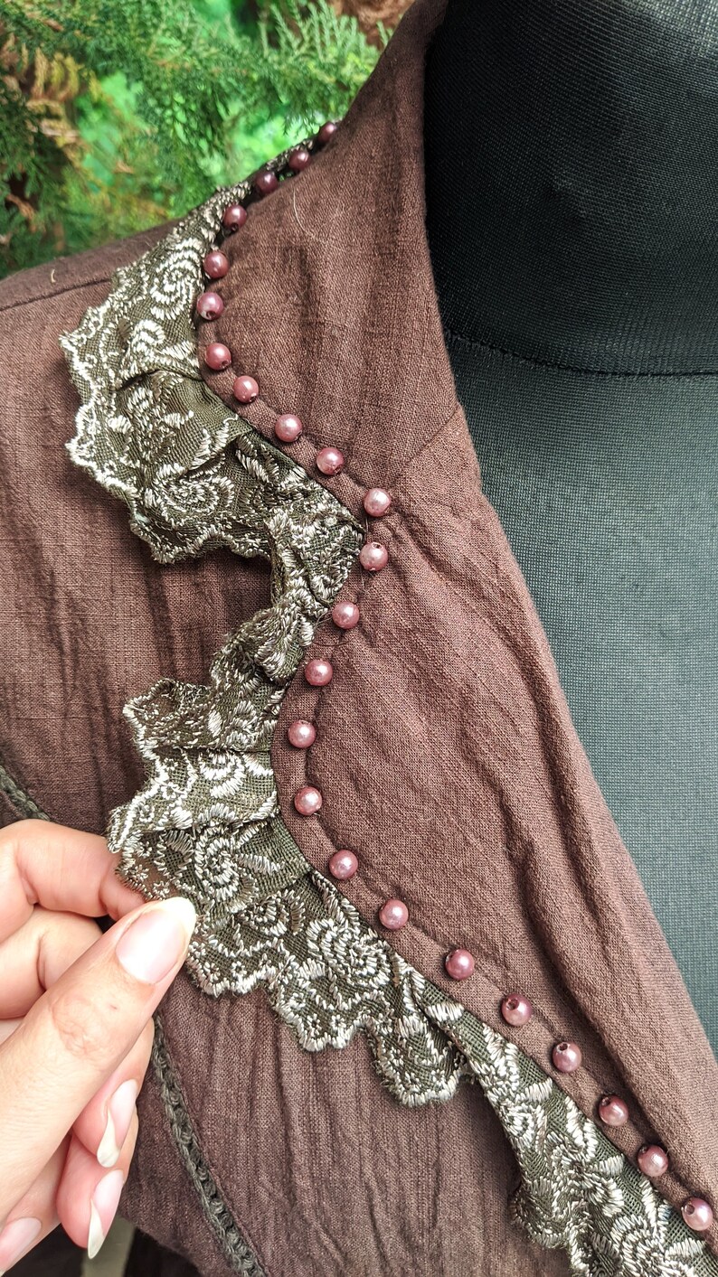 May include: A brown jacket with a lace trim and pink beads around the collar.