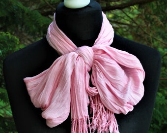 May include: A pink scarf with fringe on a black mannequin. The scarf is tied in a loose knot around the neck.