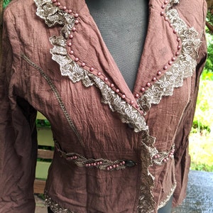 May include: A brown jacket with a lace trim and beaded accents. The jacket has a V-neck and long sleeves.
