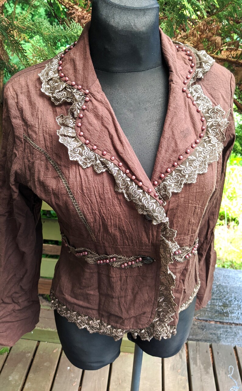 May include: A brown jacket with a lace trim and beaded accents. The jacket has a V-neck and long sleeves.