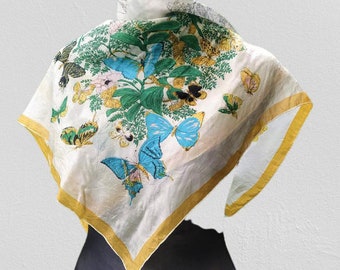 Könnte beinhalten: Ein weißer Seidenschal mit gelbem Rand und einem bunten Schmetterlingsdruck. Die Schmetterlinge sind blau, grün, gelb und rosa.
