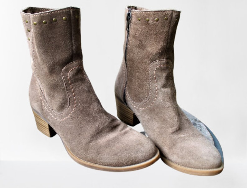 May include: A pair of brown suede ankle boots with decorative stitching and gold studs. The boots have a low heel and a pointed toe.