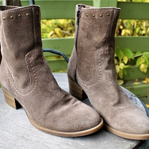 May include: A pair of brown suede ankle boots with a zipper on the side and decorative studs on the top. The boots have a block heel.