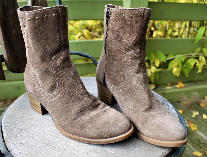 May include: A pair of brown suede ankle boots with a zipper on the side and decorative studs on the top. The boots have a block heel.