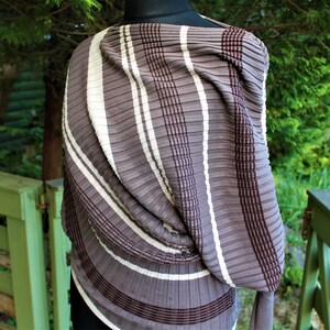 May include: A brown and white striped knit scarf with a textured, pleated design. The scarf is draped over a mannequin.