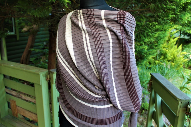 May include: A brown and white striped knit scarf with a textured, pleated design. The scarf is draped over a mannequin.
