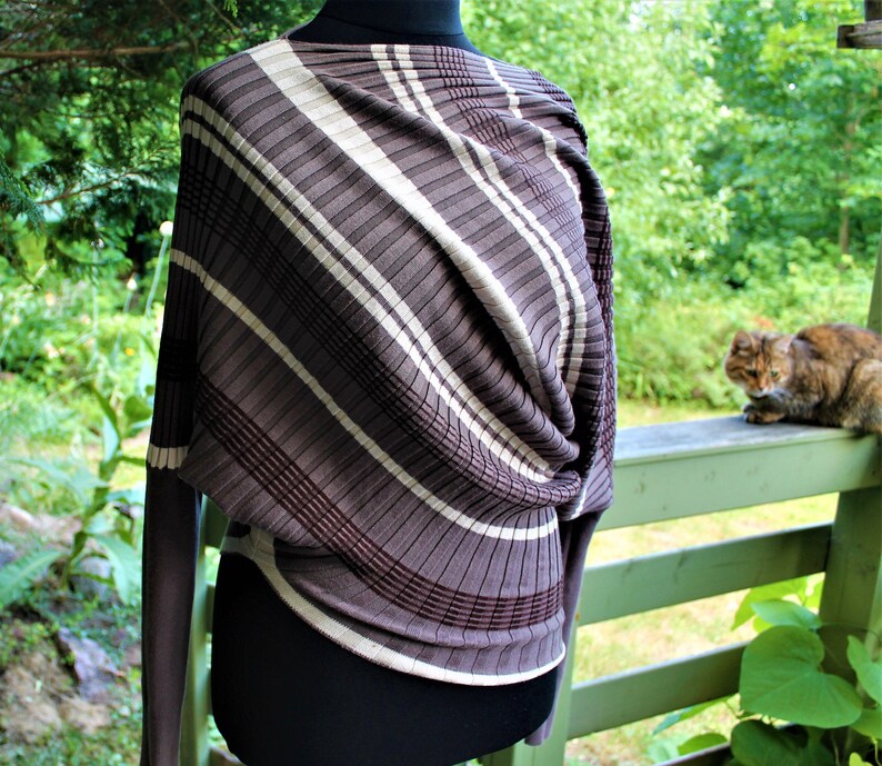 May include: A brown and white striped sweater with a twisted front detail. The sweater is on a mannequin and has long sleeves.