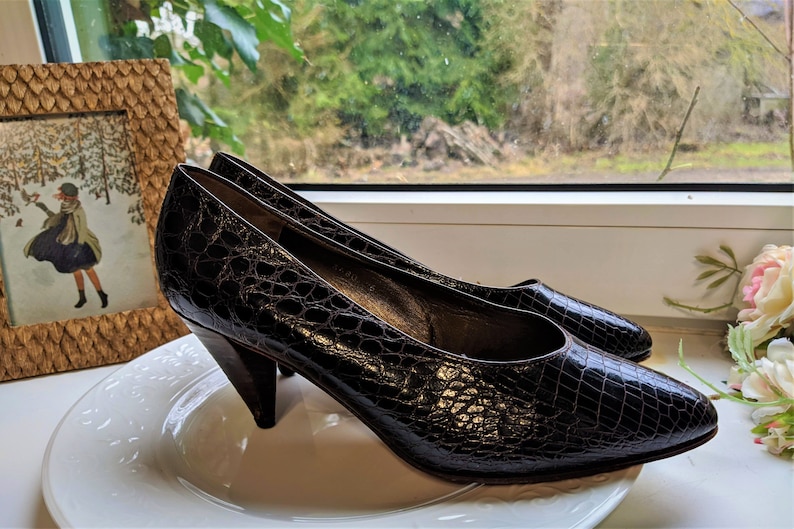 May include: A pair of brown leather pumps with a pointed toe and a low, angled heel. The shoes are on a white plate.