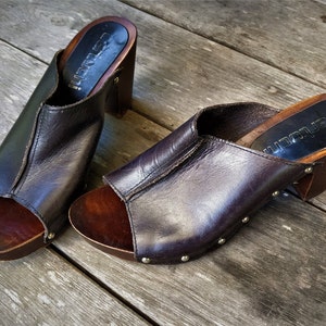 May include: Pair of brown leather heeled clogs with wooden platforms and silver studs. The clogs have a peep toe and are labelled "Lauren"