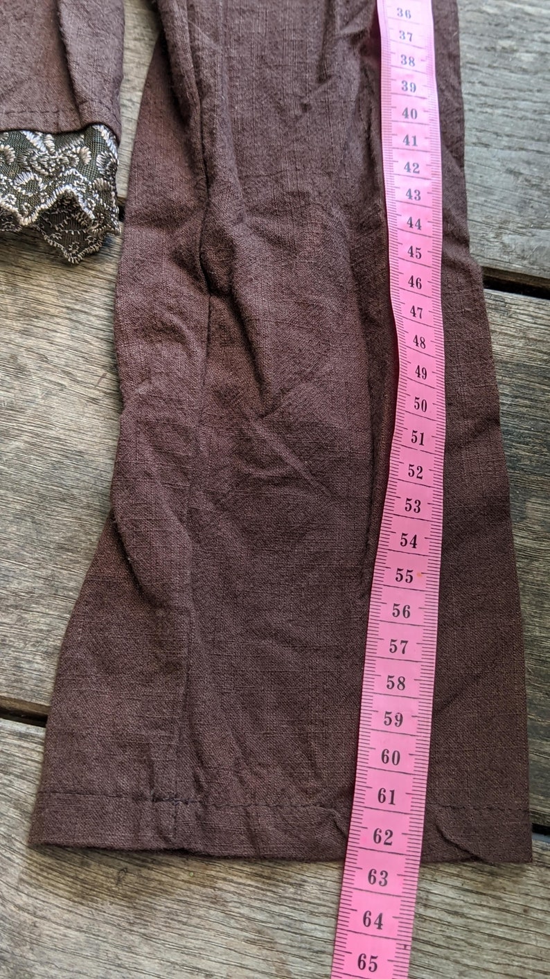 May include: A brown fabric sleeve with a lace trim. The sleeve is measured with a pink tape measure that reads from 36 to 65 inches.
