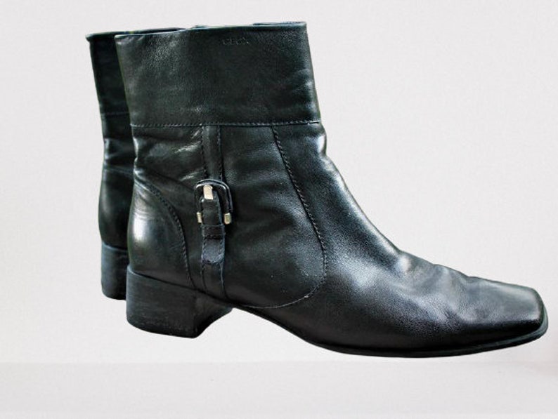 May include: A pair of black leather ankle boots with a buckle detail on the side. The boots have a square toe and a low heel.