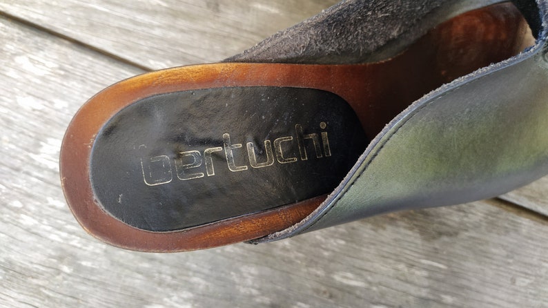 May include: Close-up of the insole of a black leather shoe with a brown wooden sole. The brand name "Berttucci" is printed in gold lettering on the insole.