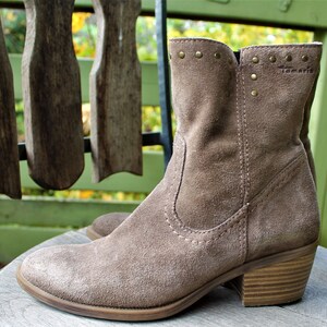 May include: A pair of brown suede ankle boots with a low block heel. The boots have a decorative row of gold studs around the top of the shaft and the brand name "Tamaris" is visible on the side.