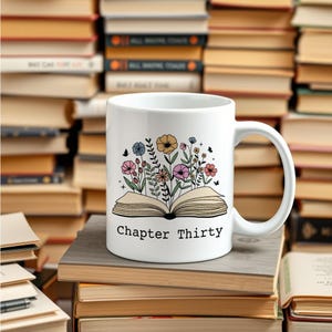 May include: White ceramic mug featuring a colourful floral design emerging from an open book. The text "Chapter Thirty" is printed on the mug.