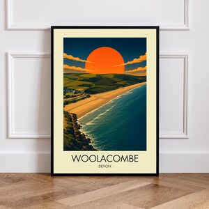May include: A framed vertical art print featuring a coastal landscape of Woolacombe, Devon. The scene depicts a sandy beach, deep blue ocean, and rolling green hills under a large, vibrant orange sun in a dark sky. The text reads WOOLACOMBE DEVON.