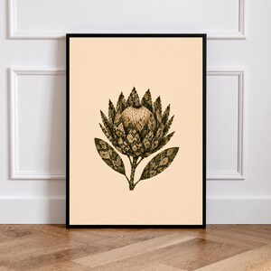 Könnte beinhalten: Ein gerahmter Kunstdruck mit einer detaillierten botanischen Illustration einer Protea-Blüte. Die Blüte hat dunkle, strukturierte, schuppenartige Blütenblätter in Braun- und Grüntönen vor einem einfarbigen, hell cremefarbenen Hintergrund.