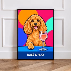 Könnte beinhalten: Ein gerahmter Kunstdruck mit einem goldbraunen, lockigen Hund, der an einem blauen Tisch neben einem Glas Roséwein sitzt. Der Hintergrund ist im Pop-Art-Stil mit orangefarbenen, pinken und türkisfarbenen Kreisen gestaltet. Unten steht ROSÉ & PLAY.