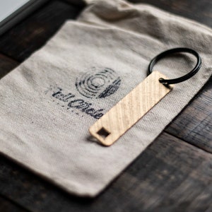 May include: A gold-colored metal keychain with a textured surface and a black metal ring. The keychain is on a white fabric pouch with the text "The Circle" printed on it.