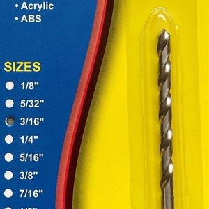 May include: A silver drill bit packaged on a yellow and blue card with the text "CRAFTICS PLAS-DRILL BIT". The card lists the drill bit sizes from 1/8 inch to 1/2 inch. The card also lists the materials the drill bit is designed for, including polycarbonate, laminates, styrenes, acrylic, and ABS. The card states that the drill bit is designed for hand drills and will not crack or chip plastic.