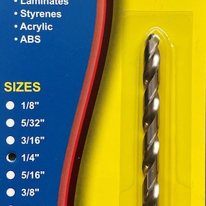 May include: A silver drill bit packaged on a yellow and blue card. The card lists the drill bit sizes from 1/8 inch to 1/2 inch. The card also lists the materials the drill bit can be used on, including polycarbonate, laminates, styrenes, acrylic, and ABS. The card reads "Craftcs Plas-Drill Bit" and "Special Design".