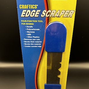 May include: A blue and yellow plastic package with a black and silver edge scraper tool. The package says "CRAFTICS EDGE SCRAPER FOUR-FUNCTION TOOL FOR EDGING: Acrylic, Polycarbonate, Styrenes, ABS, Other Plastics, Removes saw cuts, Bevels thick material, Bevels thin material, Creates rounded edge".