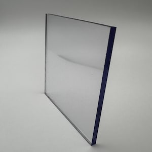 May include: A clear, rectangular sheet of transparent plastic. The edges are a dark blue color. The sheet is angled slightly, showing its thickness and clarity. The background is a plain, light gray.