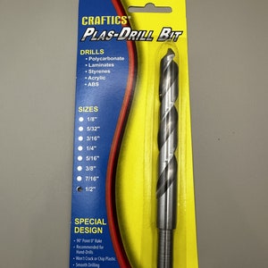 May include: A yellow and red packaging card for a CRAFTICS PLAS-DRILL BIT drill bit. The drill bit is silver and has a 90° point 0° rake design. The packaging card lists the drill bit's sizes, materials it can drill, and special design features. The card also states that the drill bit is made in the USA.