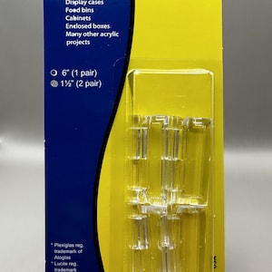 May include: A package of clear acrylic hinges for building display cases, food bins, cabinets, and other acrylic projects. The package includes two sizes: 6 inches (1 pair) and 1 1/2 inches (2 pair). The package is yellow with blue text and a white circle with a black dot in the center. The text on the package reads "Acrylic Hinges" and "Craftcs Tools and Accessories for Working with Plastic".