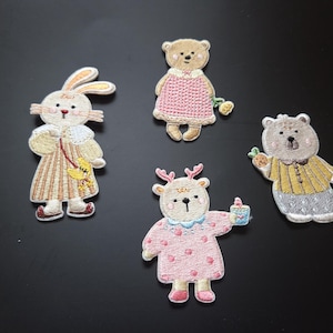 Puede incluir: Parches bordados con cuatro adorables personajes de animales: un conejo, un oso con una flor, un ciervo con una bebida y un oso con una zanahoria. Cada parche está intrincadamente detallado con varios colores y texturas, perfecto para añadir a ropa o accesorios.