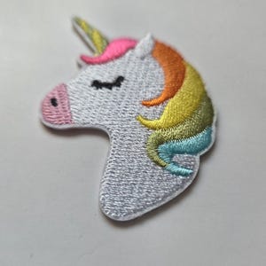 Puede incluir: Parche bordado de unicornio con cabeza blanca, nariz rosa, ojos negros y melena arcoíris. El cuerno es amarillo y la melena pasa de naranja a amarillo a azul. Ideal para decorar ropa o accesorios.