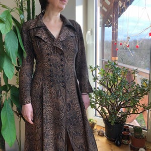 May include: A long-sleeved dress with a snakeskin print in brown and black. The dress has a V-neckline, a button-up front, and a long skirt with a slit in the front.