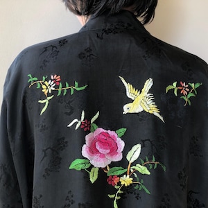 May include: Black kimono-style robe with embroidered floral and bird designs. The embroidery features pink, yellow, green, and white colors. The robe has a subtle floral pattern in the fabric.