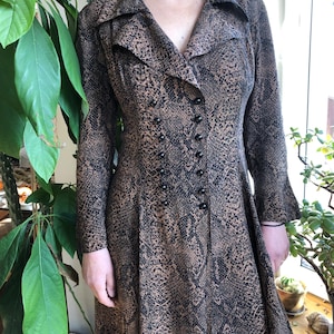 May include: A long brown and black snakeskin print dress with a V-neckline and a double breasted button closure.