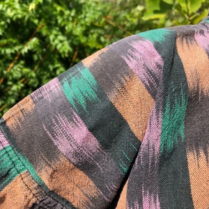 May include: Close-up of a black, brown, pink, and green patterned fabric. The fabric has a woven texture and a striped design.