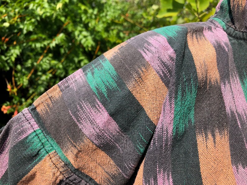 May include: Close-up of a black, brown, pink, and green patterned fabric. The fabric has a woven texture and a striped design.
