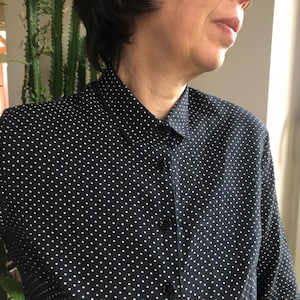 Puede incluir: Una camisa negra con lunares blancos. La camisa tiene un cuello clásico y está abotonada. La tela parece ser ligera, ideal para climas cálidos.