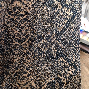 May include: Close-up of a brown fabric with a black snake skin pattern. The fabric has a small hole in the center.