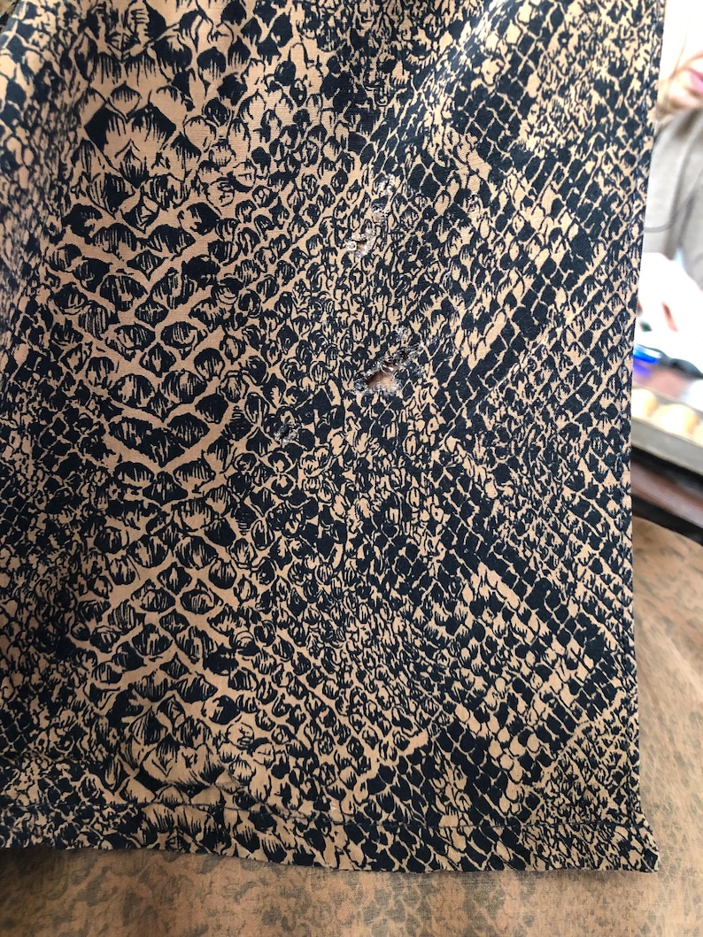May include: Close-up of a brown fabric with a black snake skin pattern. The fabric has a small hole in the center.
