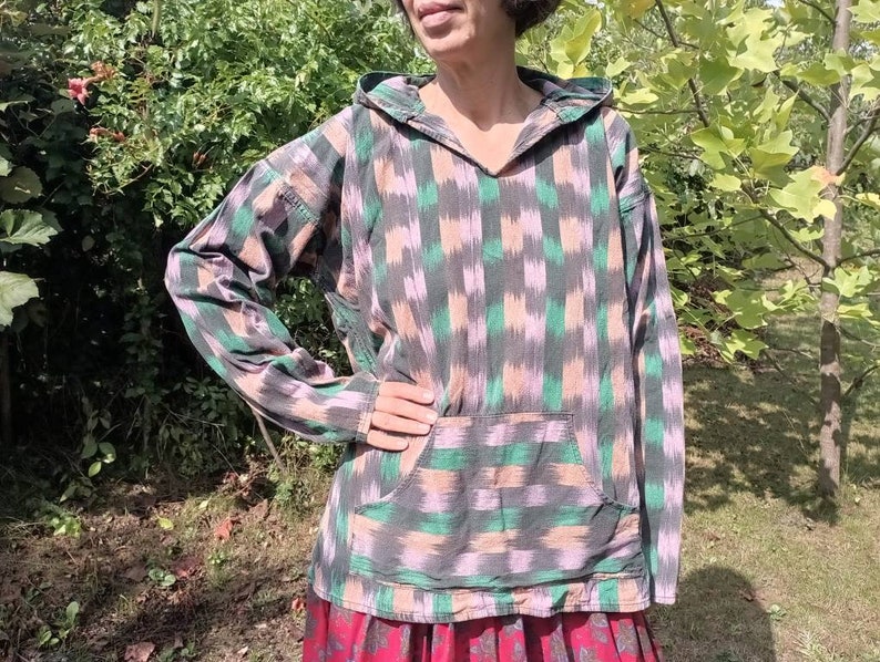 May include: A hooded sweatshirt with a green, pink, and black ikat pattern. The sweatshirt has a kangaroo pocket and long sleeves.