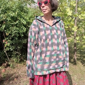 May include: A hooded sweatshirt with a green, pink, and black geometric pattern. The sweatshirt has a large pocket on the front and a drawstring hood.