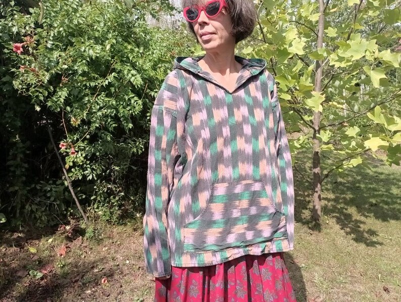 May include: A hooded sweatshirt with a green, pink, and black geometric pattern. The sweatshirt has a large pocket on the front and a drawstring hood.