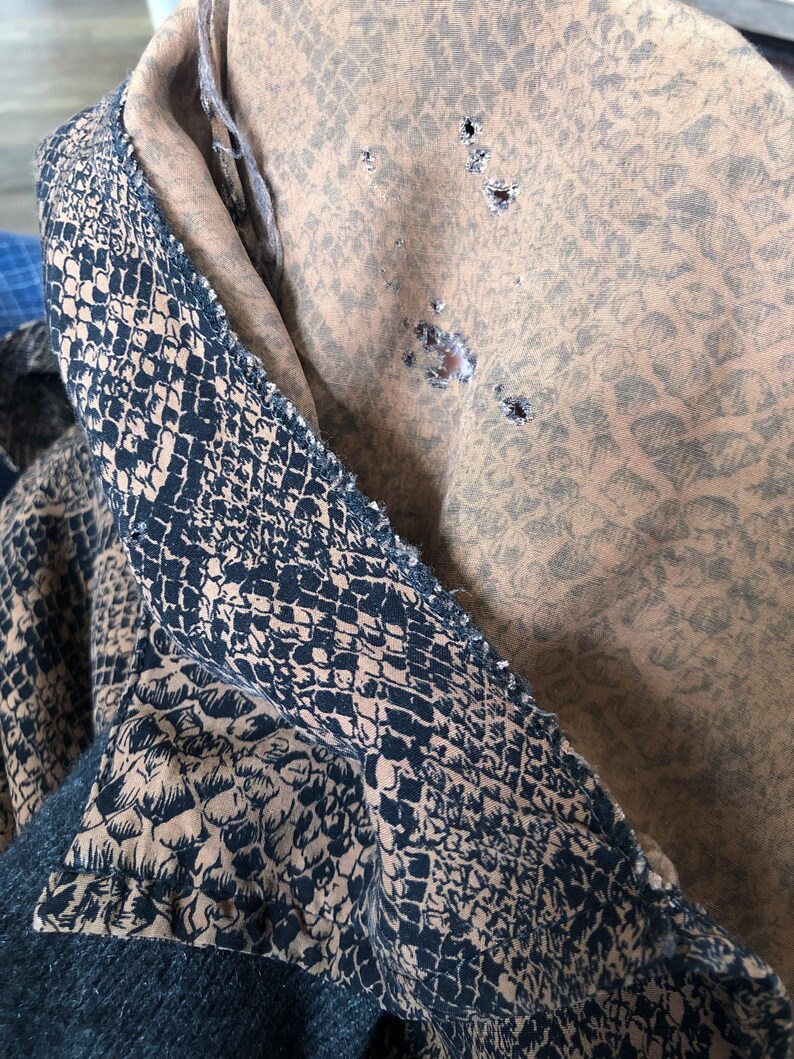 May include: A close-up of a brown fabric with a snake skin pattern. The fabric has several small holes in it.