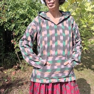 May include: A hooded pullover with a geometric pattern in shades of green, pink, and black. The pullover has a kangaroo pocket and a relaxed fit.