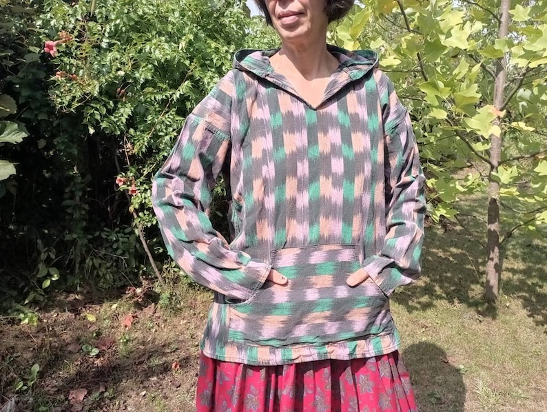 May include: A hooded pullover with a geometric pattern in shades of green, pink, and black. The pullover has a kangaroo pocket and a relaxed fit.