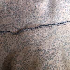May include: Close-up of a brown fabric with a snakeskin pattern. The fabric has a black seam running across the middle and several small holes along the seam.