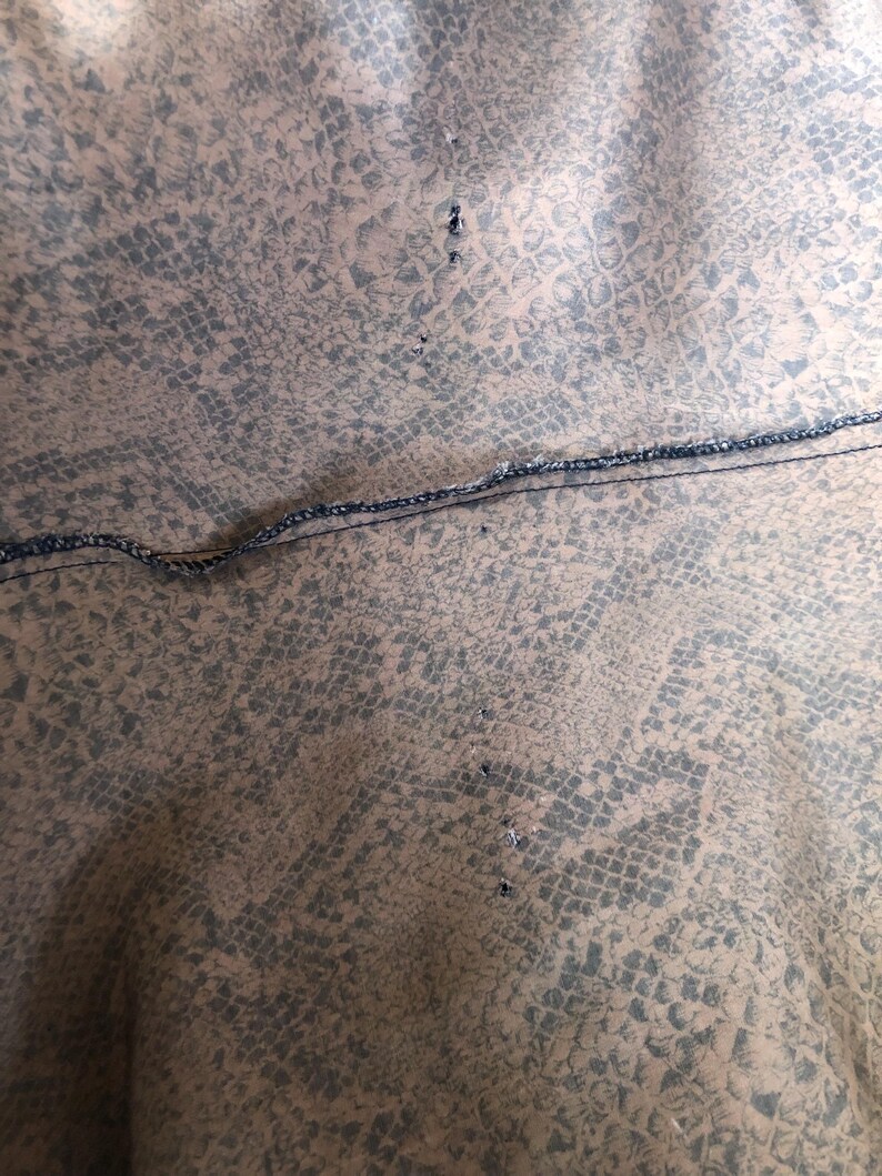 May include: Close-up of a brown fabric with a snakeskin pattern. The fabric has a black seam running across the middle and several small holes along the seam.