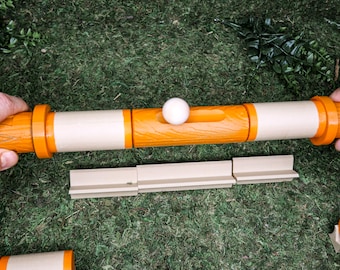 Könnte beinhalten: Ein Holzspiel mit orangefarbenen und beigen Abschnitten. Eine weiße Kugel ruht auf der Oberseite des Spiels. Das Spiel besteht aus mehreren Teilen, die auf verschiedene Weise zusammengesetzt werden können.