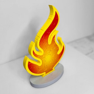 May include: A wooden puzzle in the shape of a flame. The puzzle is made up of many small pieces that fit together to form the shape of a flame. The flame is painted in shades of yellow, orange, and red.