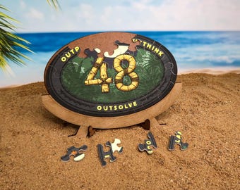 Könnte beinhalten: Ein Holzpuzzle mit einem braunen Rahmen und einem grünen und braunen Puzzleteil im Inneren. Das Puzzleteil trägt die Nummer 48 und die Worte "Outthink, Outsolve". Unter dem Puzzle liegen fünf kleinere Puzzleteile auf dem Sand.